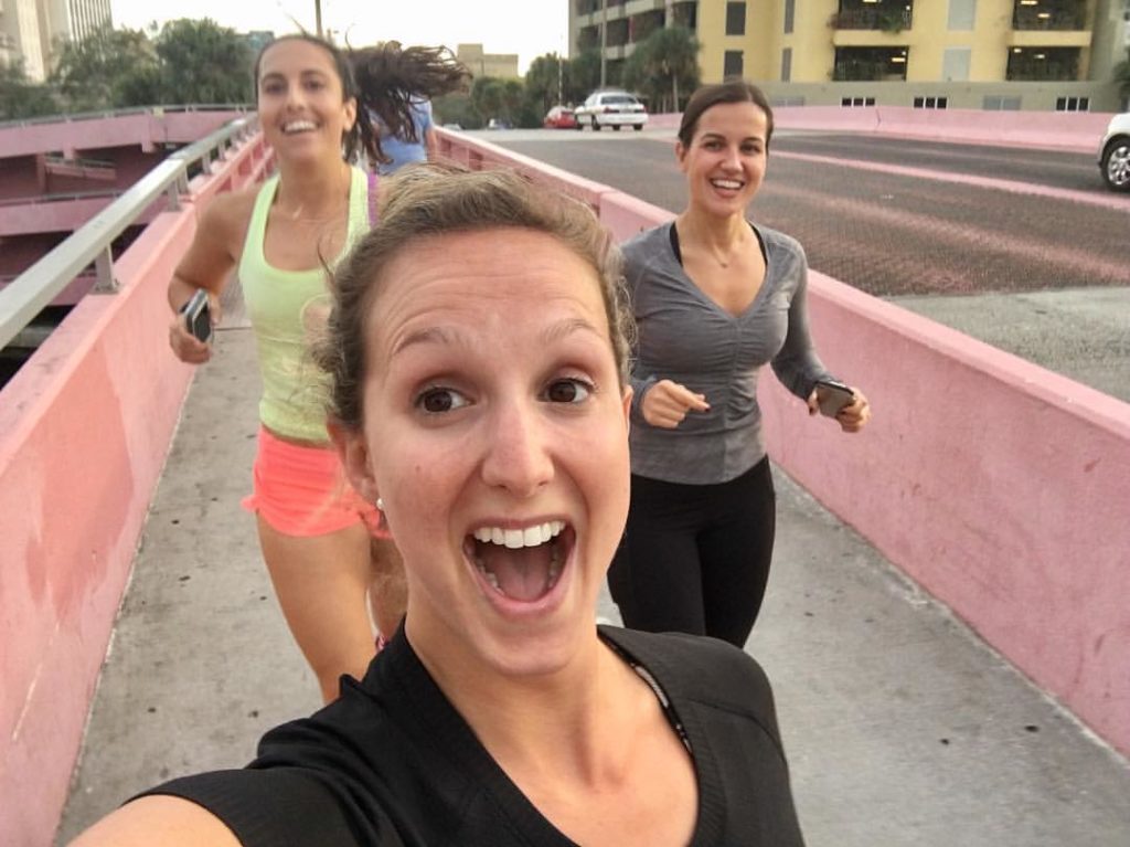 Cristina Ramirez, running, taking a selfie with two friends behind her, with a giant, open-mouth smile on her face. 