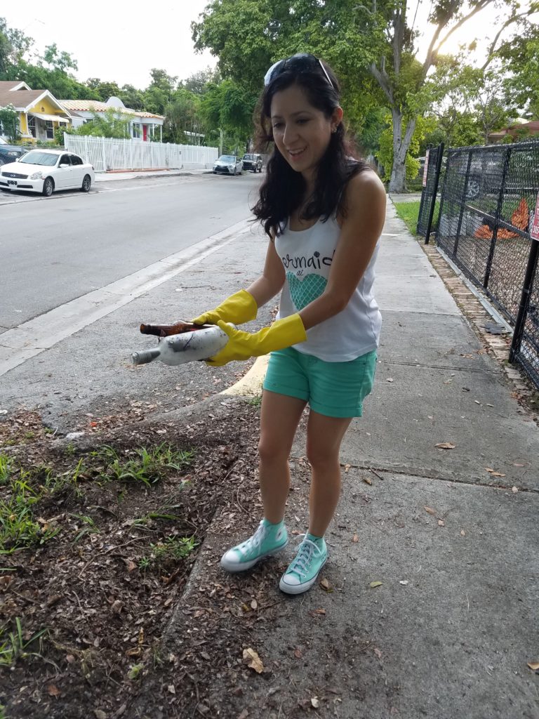Lilia wears yellow rubber gloves as she picks up garbage from a planter in the urban area of Wynwood. 