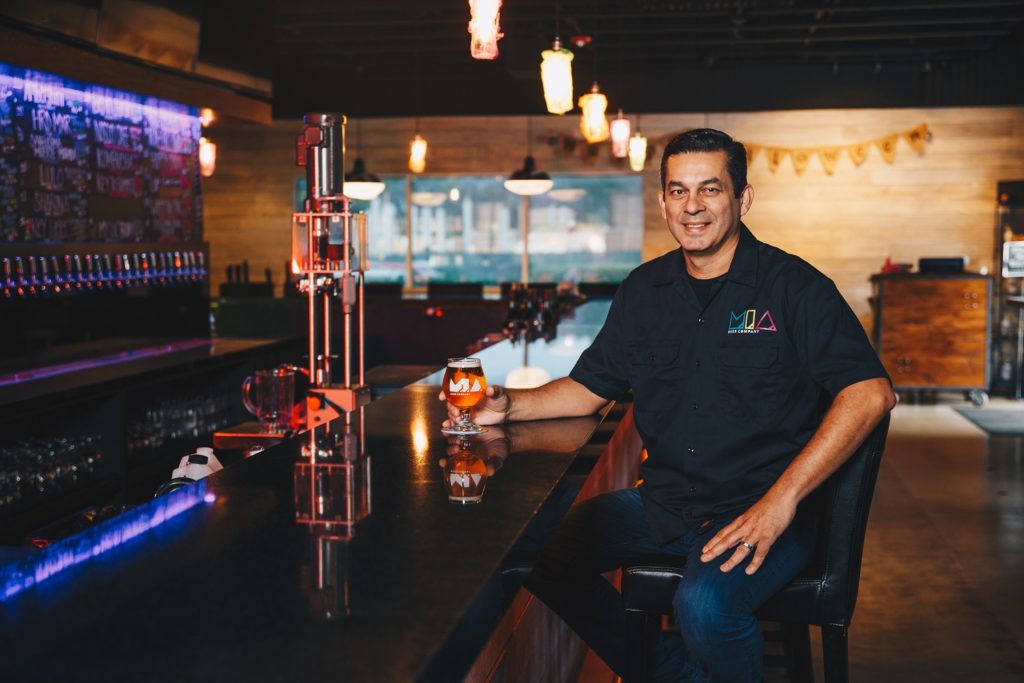 Eddie Leon, co-founder of MIA Beer Company, sits at the bar in the taproom, with a glass of MIA Beer in his hand. 