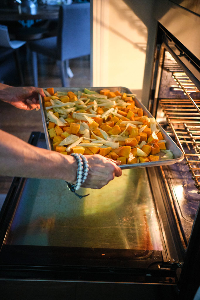 Chef Julie's hands are seen putting a pan of butternut squash an fennel  into the oven. 