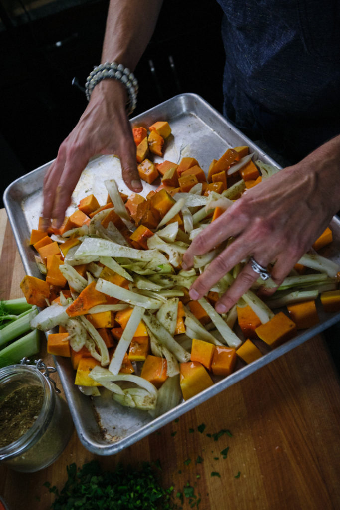 Chef Julie's hands are seen tossing the butternut squash and fennel chunks with za'atar seasoning. 