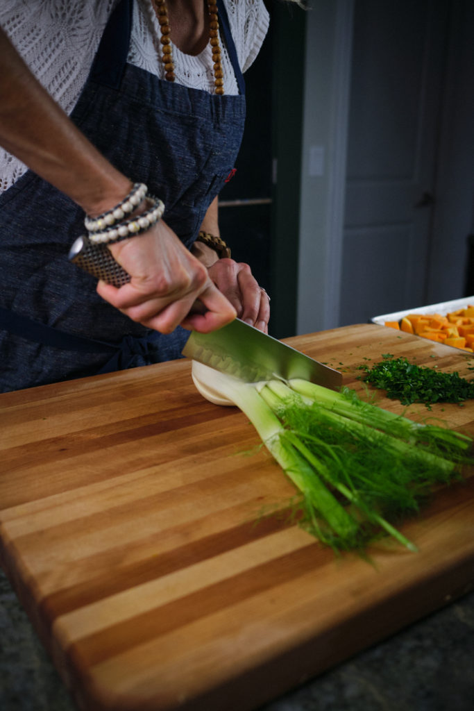 Chef Julie's hands are seen chopping a fennel bulb on a wooden cutting board. 