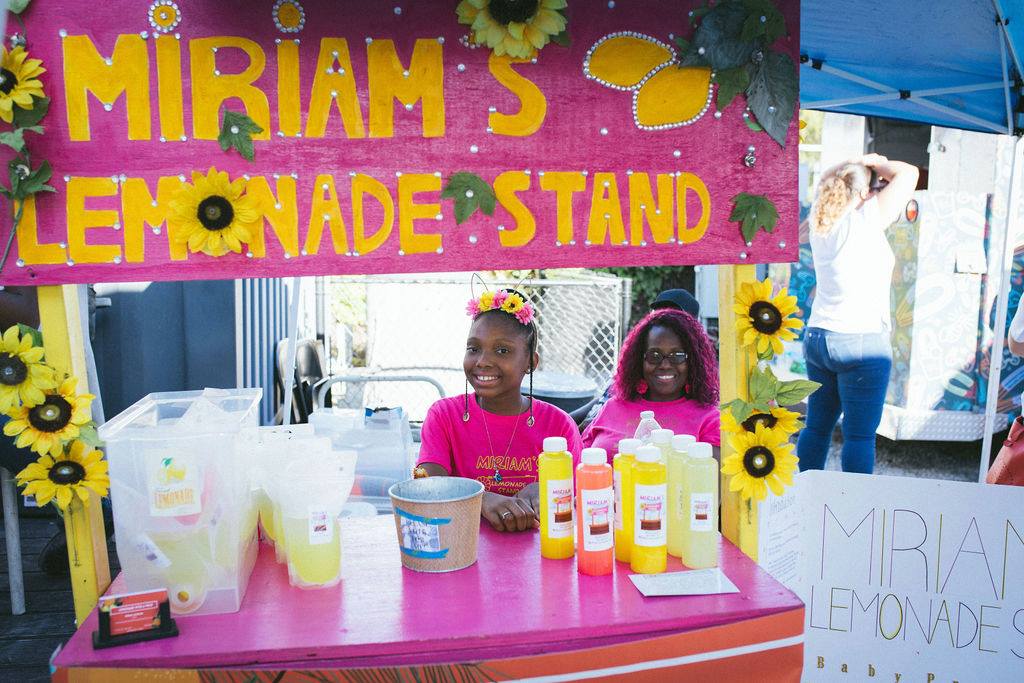 Miriam sits at her brightly colored lemonade stand, waiting for business. 