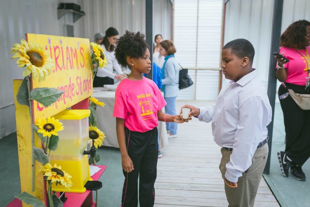 Miriam hands a sample cup of her lemonade to a young patron.