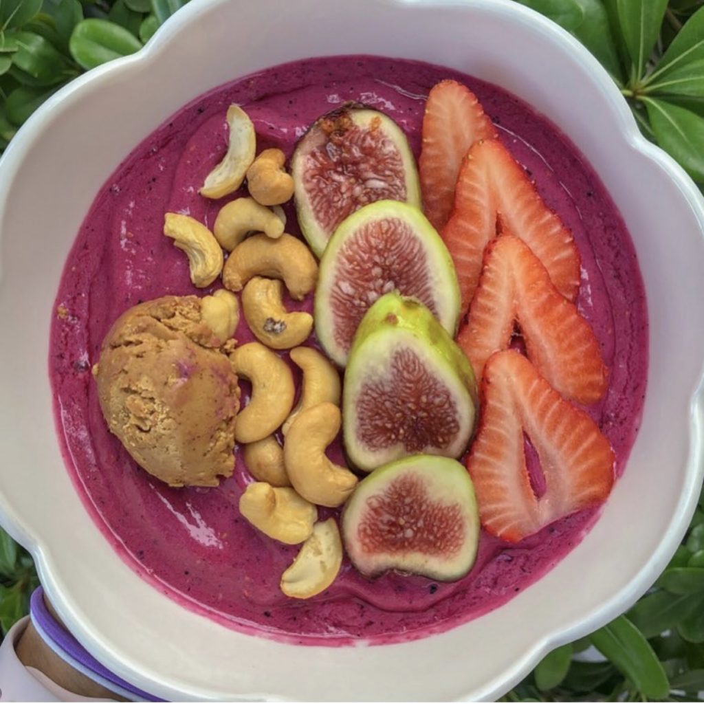 bowl full of fresh fruits and cashews on top of a vibrant dragolfruit smoothie