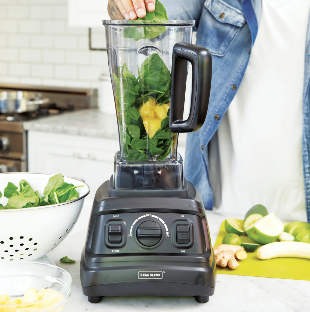 Person fills a blender with spinach and fruit to make a smoothie.