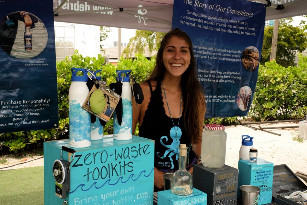 A smiling young woman stands at her information booth with zero-waste kits for sale. 