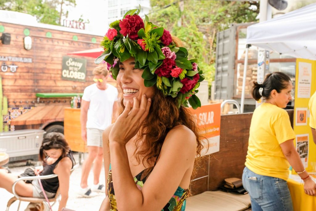 A smiling woman wears a large Polynesian flower crown.