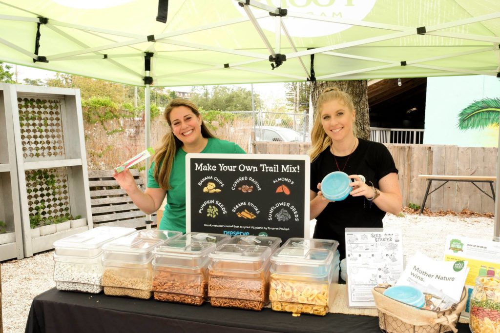 Two women stand behind a booth with clear bins of nuts and other trail mix ingredients. 