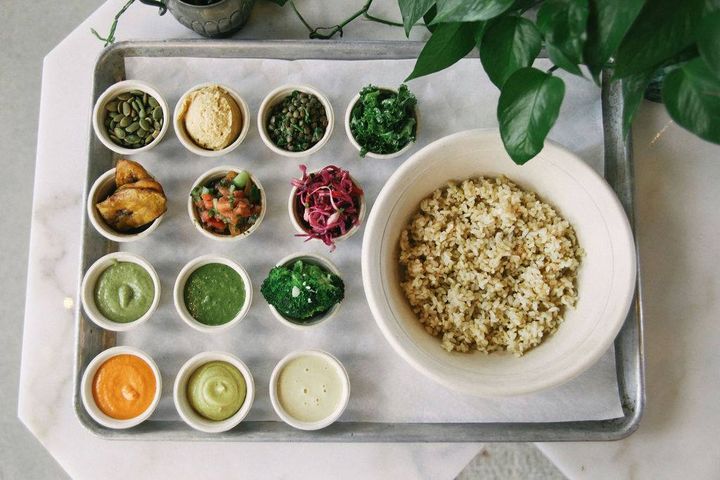 della bowls sauces and vegetable toppings arranged in mise en place around a bowl of brown rice