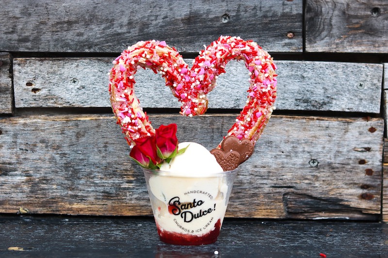 Santo Dulce! Churros Valentine's Day churro in the shape of a heart with red sprinkles nestled in a scoop of vanilla ice cream and garnished with heart-shaped chocolates and a rose